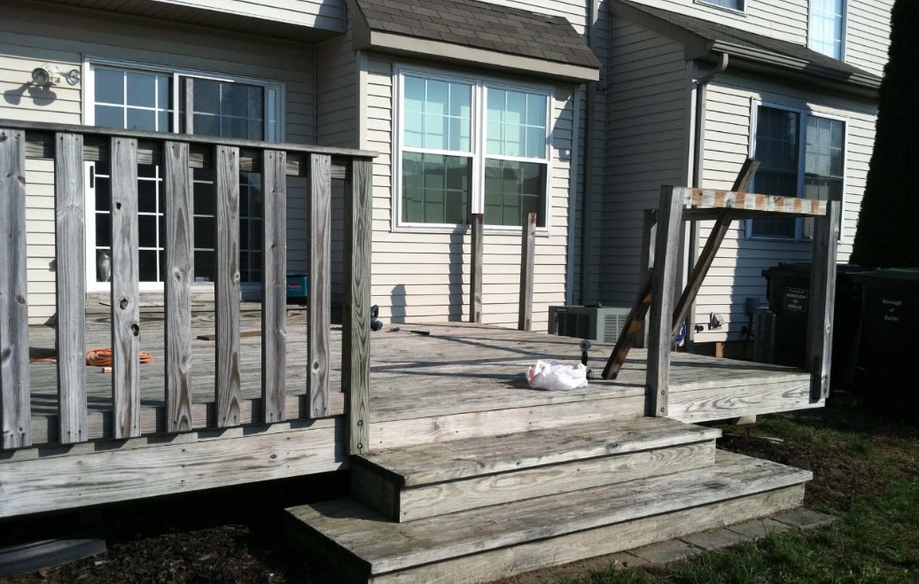 Before - weathered gray wooden deck with broken railings